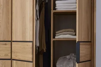 Geöffneter Kleiderschrank aus Massivholz, mit Regalböden, die mit T-shirts befüllt sind.