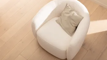 Gemütlicher weißer Boucle Sessel mit einem beigen Kissen, der von der Sonne gestreift wird.