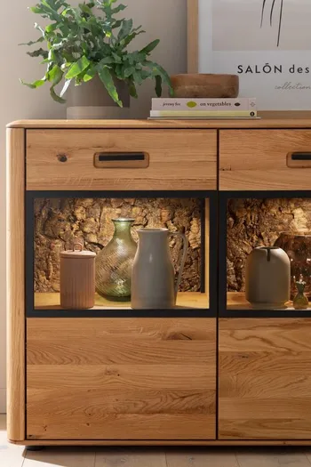 Sideboard mit beleuchteten Glasfächern und Korkeichenrinde an der Rückwand.