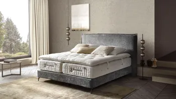 Modernes graues Boxspringbett mit Stoffbezug, auf dem zwei Sleepeezee Matratzen liegen, darüber ein Topper und Kissen in weiß und beige.