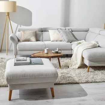 Weißes Ecksofa aus Cord gemütlich dekoriert mit hellen Kissen und Decken mit einem passenden Hocker und einem braunen dreieckigen Beistelltisch.