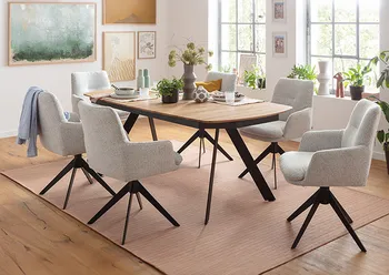 Moderner Essbereich mit Massivholztisch in Eicheoptik und schrägen Metallbeinen, umgeben von sechs gepolsterten, drehbaren Armlehnstühlen in hellem Stoff – stilvoller Esszimmer-Look mit gemütlichem Ambiente und viel Tageslicht.