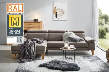 Siegel &quot;Goldene M&quot; auf einem Bild von einem Braunen Ecksofa mit klappbaren Kopfstützen und Armlehnen in einem hellen Wohnzimmer mit großem Fenster.