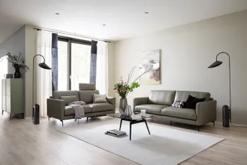 Zwei moderne graue Ledersofas, die im rechten Winkel zueinander stehen und große bequeme Rückenkissen haben, das linke Sofa hat eine Kopfstütze über dem rechten Polster.