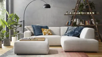 Modernes beiges Ecksofa mit Cordstoff bezogen und einem passenden Hocker, auf dem Sofa sind mehrere Kissen in blau und gelb.