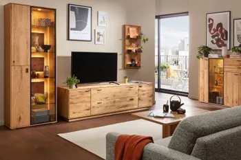 Wohnwand aus aus Eiche bestehend aus einer Vitrine mit beleuchteten Glaseinsätzen, TV-Board, hängendes Wandregal und einem Sideboard mit Glaseinsätzen in einem hellen gemütlichen Raum.