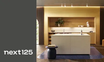 Minimalistische weiße Küche mit Insel und Einbauschrank von next125. Im Bild das Logo von next125 auf grauem Hintergrund.  