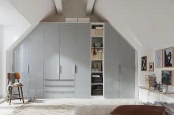 Weißer großer Kleiderschrank, der maßgeschneidert zwischen zwei Wänden mit Dachschräge steht.