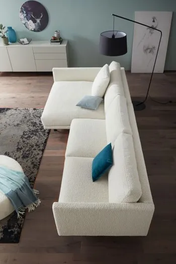 Ansicht von oben auf ein großes weißes Ecksofa mit großen Rückenkissen und blauem, grauen und weißem Dekokissen.