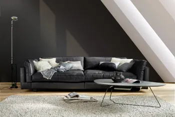 Modernes großes schwarzes Ledersofa mit hohen dick gepolsterten Armlehnen vor einer schwarzen Wand.