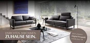 Wohnzimmer mit zwei Sofas; Claim „Zuhause sein“ und Digital-Prospekt-Link.