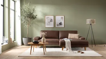 Modernes braunes Leder Ecksofa mit Holzbeinen in einem hellen gemütlichen Wohnzimmer mit großer Pflanze.