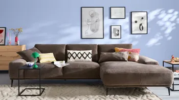 Helles Wohnzimmer mit großem dunkelbraunen Ecksofa und zwei Designder-Beistelltischen und einer Kommode.