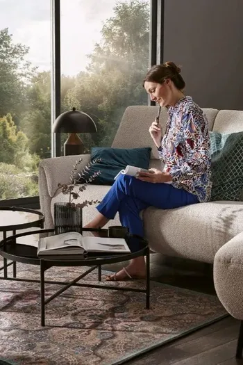 Frau sitzt gemütlich auf einem beigen Sofa mit hoher Rückenlehne.