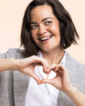 Lächelnde Frau formt Herz mit Händen, sympathisches Porträt für Couchliebe Lounge.