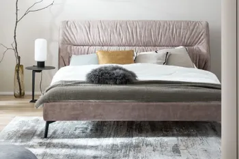 Beiges Design Polsterbett mit einer Querfalte am Kopfteil und mehreren Kissen in beige, gelb, und schwarz und Decken in weiß und grün.