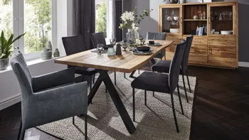 Massivholz Esstisch mit Gestell aus schwarzem Metall, um den herum Stühle in grautönen mit und ohne Armlehne stehen in einem gemütlichen Esszimmer mit beigem Teppich und Massivholz Highboard.
