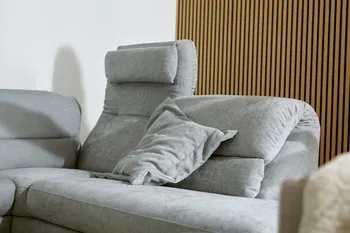 Graues Ecksofa aus Stoff, bei dem eine Rückenlehne hochgeklappt ist und eine umgeklappt, mit einem grauen Kissen.
