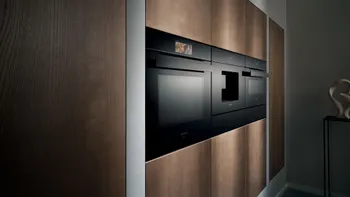 Schwarzer Backofen, schwarzer integrierter Kaffeevollautomat und schwarzer Kompaktbackofen mit Mikrowellenfunktion erhöht eingebaut mit braunen Küchenfronten