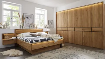 Massivholzbett mit integrierter Beleuchtung und Nachtkonsolen neben einem großen Massivholz Kleiderschrank.