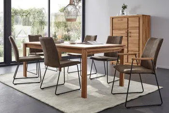 Gemütliches Esszimmer mit einem Esstisch aus Massivholz, der auf einem weißen Teppich steht, brauenen Stühlen mit schwarzem Metallgestell mit und ohne Armlehne und einem Highboard aus Massivholz.