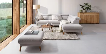 Weißes Ecksofa aus Cord mit passendem Hocker dekoriert mit weißen Kissen in einem gemütlichem hellen Wohnzimmer mit großer Fensterfront.