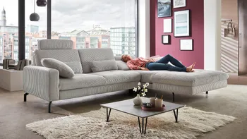 Frau liegt auf hellgrauem Stoffsofa mit Relaxfunktion in Wohnzimmer.