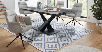 Hellgrauer Keramik Esstisch in einem hellen Raum, um den graue Schalenstühle stehen mit schwarzem Metallgestell.