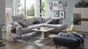 Zeitloses graues Ecksofa, das links ein extragroßes Rückenkissen mit Steppung hat in einem hellen Raum.