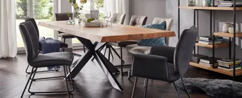 Esstisch aus Massivholz mit schwarzem Spinnenfußgestell, um den mehrere Stühle mit und ohne Armlehne in Grautönen stehen.