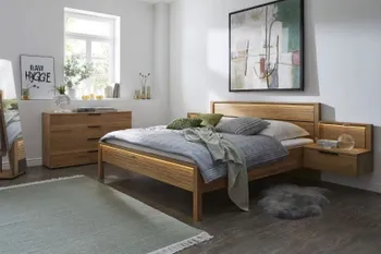 Helles Schlafzimmer mit einem Bett und hängenden Nachttischen aus Massivholz sowie einer passenden Kommode.