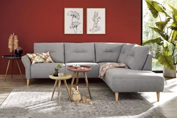 Graues Ecksofa mit Holzfüßen und bequemen dick gepolsterten Rückenkissen, mit einer Quernaht.