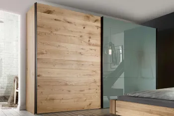 Kleiderschrank mit zwei großen Schwebetüren, von denen die linke komplett aus Massivholz ist und die rechte aus Milchglas in einem hellen Schlafzimmer.