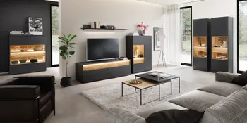 Beleuchtete anthrazitfarbene Wohnwand mit holzakzenten in gemuetlichem Wohnzimmer. 