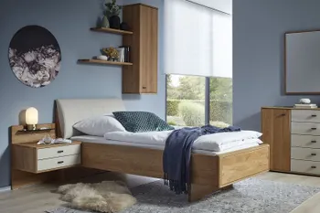 Helles Schlafzimmer mit Massivholzbett mit beigem Polster Kopfteil und dazu passende Nachttischkonsole und Sideboard mit weißen Elementen.