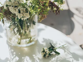 Blumen liegen auf einem runden Tisch, daneben Blumen in einer Glasvase