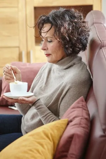 Frau sitzt auf einem weinroten Ledersofa mit einem Kaffee in der Hand.