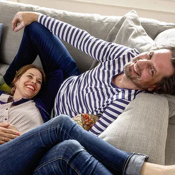 Mann und Frau die entspannt auf einem Sofa liegen und lachen.