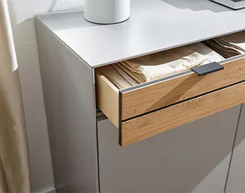 Kommode in grauem Lack mit geöffnetem Schubladen, der eine Front in Holzoptik hat und einen schwarzen Griff.