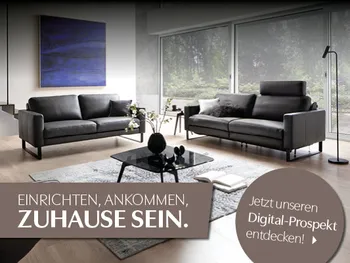 Wohnzimmer mit zwei Sofas; Claim „Zuhause sein“ und Digital-Prospekt-Link.