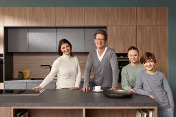 Glückliche Familie, die vor einer modernen Küche mit Holz und grauen Elementen steht.