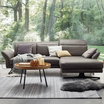 Ecksofa in grauem Leder vor einer großen Fensterfront mit Blick ins grüne.