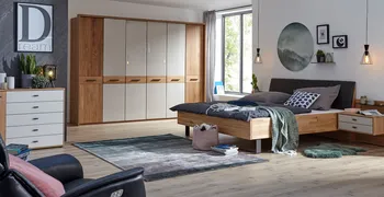 Helles Schlafzimmer mit Massivholz Bett und großem Kleiderschrank mit weißen Elementen.