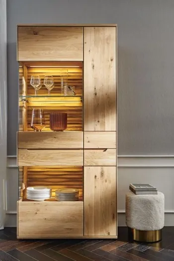 Große Vitrine aus Massivholz mit beleuchteten Glaseinsätzen und auffälliger Rückwand in einem hellen Raum.