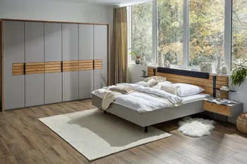 Kleiderschrank in grauem Lack und mit Elementen aus Naturholz neben einem Bett, dessen Rahmen in grauem Lack lackiert ist und Nachttisch und Kopfteil mit Massivholzelementen.