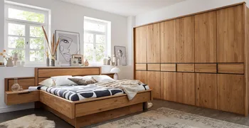 Massivholzbett mit integrierter Beleuchtung und Nachtkonsolen neben einem großen Massivholz Kleiderschrank.