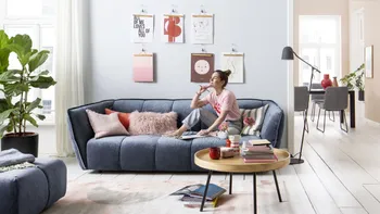 Gestepptes blaues Sofa mit Samtbezug, auf dem eine Frau sitzt und nachdenklich wirkt.