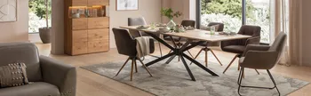 Modernes Esszimmer mit einem Massivholztisch, Schalenstühle in grau und braun vor einem großen Fenster mit vielen grünen Pflanzen.